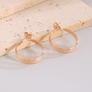 Macro detail of rose gold C-shaped wheat pattern earrings on a textured stone