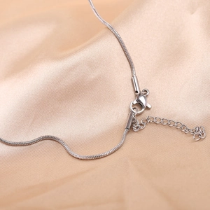 Detailed close-up of a silver snake chain necklace with lobster clasp on silk fabric