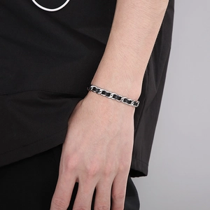 Gros plan d'un bracelet en cuir tressé noir avec chaîne en acier argenté au poignet