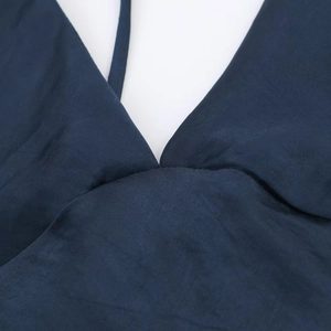Détail macro d'une robe en satin bleu foncé montrant le col en V et les fines bretelles