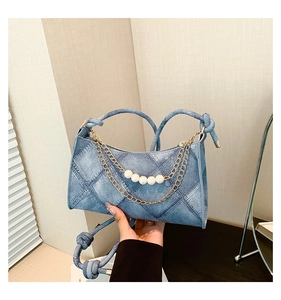 Détail du sac croissant en denim bleu avec coutures matelassées et chaîne de perles