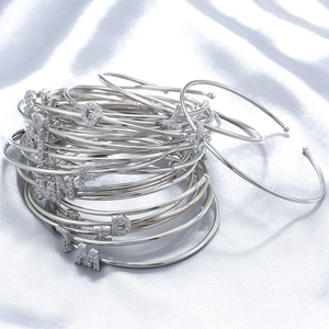 Polished silver letter bangles with sparkling zircon charms on white silk fabric