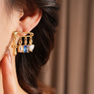 Macro side view of gold safety pin earrings with zircon cross and heart on ear