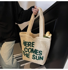 Detailed close-up of woven straw tote bag with green Here Comes The Sun embroidery