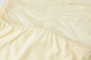 Detail of light yellow mesh fabric featuring vertical ruched design and sheer texture