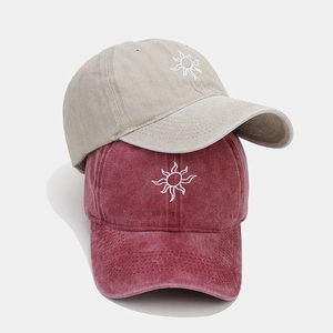 Detail of retro washed cotton baseball caps with sun embroidery in beige and burgundy