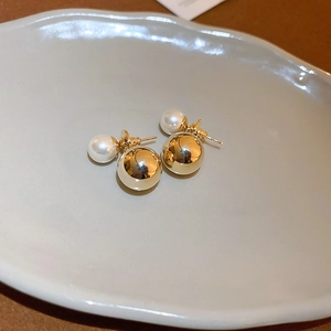 Detail of gold-plated double-ball stud earrings with a white pearl and polished gold sphere