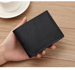 Close-up of black bifold wallet with lychee grain texture held over a wooden desk