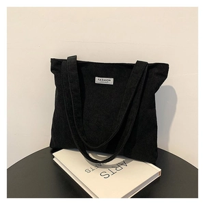 Detail of black corduroy tote bag with wide strap and fashion patch on a desk