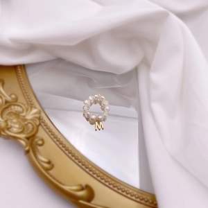Detail of freshwater pearl beaded ring with a gold letter M charm on vintage mirror
