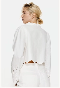 Detail of white long sleeve shirt featuring intricate hollow embroidery and ruffle edges