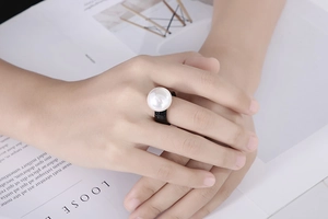 Detail view of a large white round pearl set on a wide black band ring for women