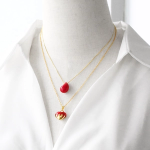 Double-layered gold necklace featuring red waterdrop and heart pendants on a white shirt
