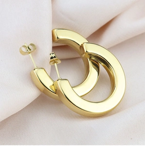 Macro shot of polished gold C-shaped hoop earrings on soft pink satin fabric background