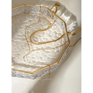 Artistic high-angle shot of layered 18k gold stainless steel necklace in glass tray