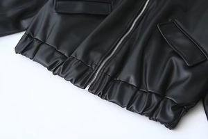 Detail of black PU leather jacket with silver zipper, flap pockets and elastic hemline