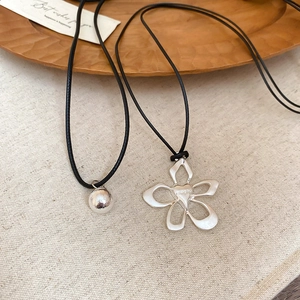 Detail of silver hollow flower pendant and round ball charm on black cord necklace