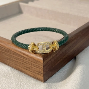 Dettaglio del bracciale in pelle intrecciata verde scuro con chiusura dorata e zirconi