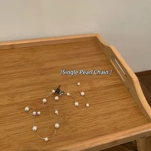 Close-up of pearl hair chain with elegant butterfly clasp on minimalist wooden tray