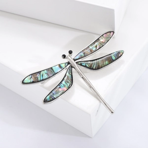Vintage dragonfly brooch in silver alloy with abalone shell wings on white pedestal