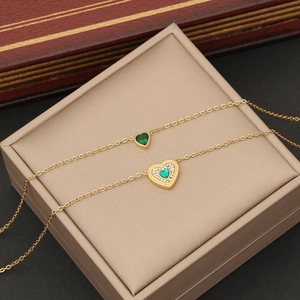 Macro shot of two gold necklaces with emerald heart pendants and shimmering crystal halos