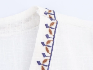 Detailed view of purple and brown leaf embroidery on white linen texture shirt fabric