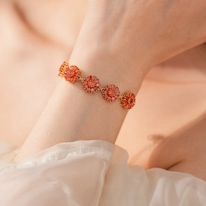 Detail of gold-plated flower bracelet featuring orange-red zircon stones on a model wrist
