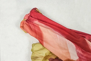 Detailed view of red and yellow gradient print fabric with elastic smocking and pleated texture
