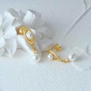 Detailed close-up of 925 silver gold pearl drop earrings on white texture background