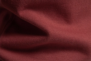 Macro shot of burgundy knit sweater fabric showing detailed combed cotton texture
