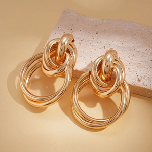 Detail view of multi-layered gold geometric hoop earrings on a beige stone pedestal