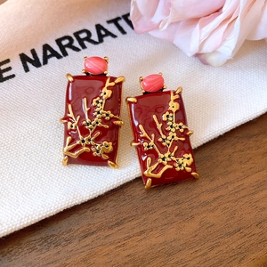 Detail of vintage red floral enamel earrings with pink cat eye stone on a textured bag