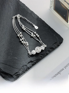 Detail of layered S925 silver beaded bracelet with engraved charms on black stone surface