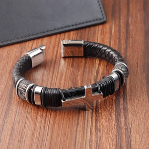 Gros plan du bracelet en cuir tressé avec breloque croix en argent sur table en bois