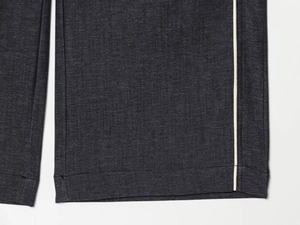 Détail du pantalon en jean gris foncé avec bandes latérales crème et finitions couture