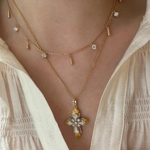 Detail of layered gold necklaces with vatican cross pendant and teardrop zircon accents