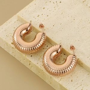 Detail of rose gold C-shaped earrings with spiral texture on light stone surface