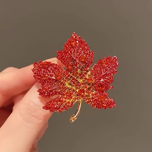 Macro shot of maple leaf brooch with red gradient rhinestones on golden metal base