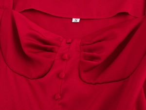 Detailopname van de rode jurk met pofmouwen en een geplooide borst met knopen