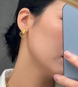 Close-up of elegant gold twisted hoop earrings with oval studs worn by a female model