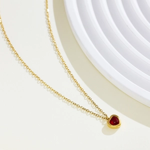 Detailed close-up of a gold-plated heart necklace featuring a vibrant red zircon pendant