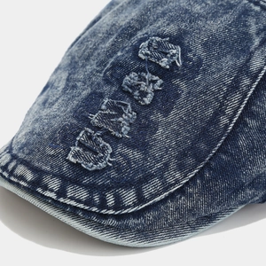 Close-up of vintage washed denim newsboy cap with white embroidered letters and stitching