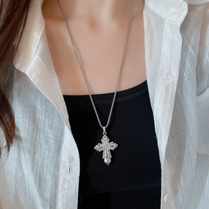 Close-up of a silver cross necklace with inlaid rhinestones worn by a fashion model