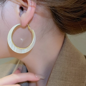 Primo piano di eleganti orecchini a cerchio dorati con inserto in madreperla bianca