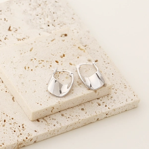 Detailed view of irregular polished silver U-shaped earrings on beige travertine stones