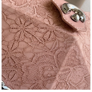 Close-up of pink lace embroidery fabric and polished silver metal buckle on a shoulder bag