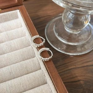 Detail of silver hoop earrings with screw-thread texture on a wooden jewelry box