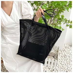 Close-up of black mesh beach bag with premium leather trim held by a model in nature