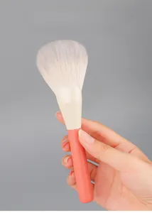 Close-up of a large fluffy fan makeup brush with orange handle held by a person