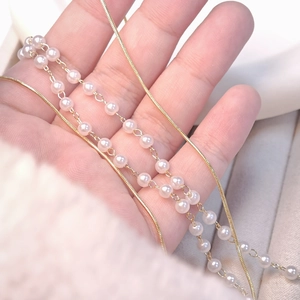 French style layered gold snake chain and white pearl necklace held in hand
